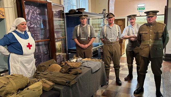 photo of men in WW1 military uniform and a woman in a nurse's uniform, demonstrating WW1 equipment.